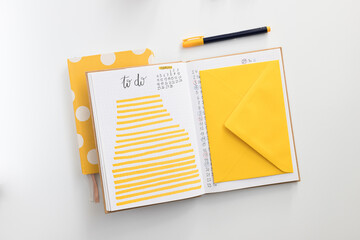 Two piled notebooks. The top one is opened and shows a to-do list for february and an illuminating yellow envelope on the right side.