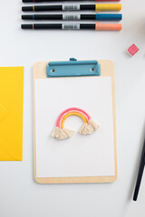 Closeup view of a clipboard with an empty sheet and a rainbow at top.
