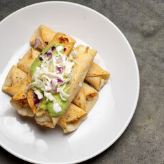 Fried tacos called flautas with guacamole and cabbage on dark background. Mexican food