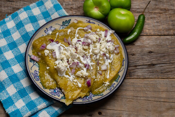 Green enchiladas with fresh cheese and sour cream on wooden background. Mexican food