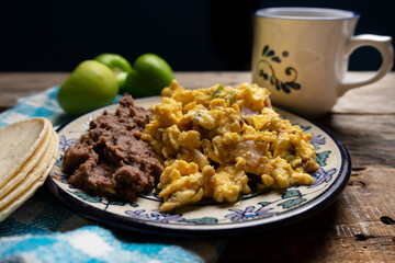 Scrambled eggs with green sauce and refried beans on wooden background. Mexican food