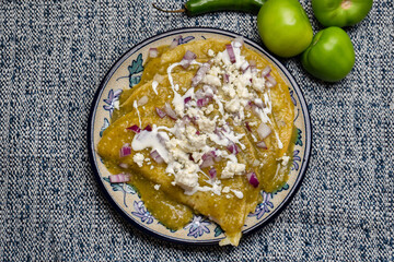 Green enchiladas with fresh cheese and sour cream on blue background. Mexican food