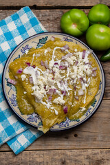 Green enchiladas with fresh cheese and sour cream on wooden background. Mexican food