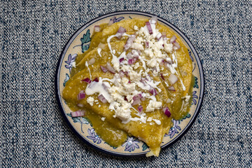 Green enchiladas with fresh cheese and sour cream on blue background. Mexican food