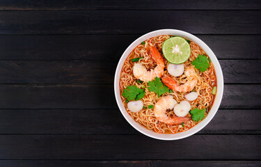 Ramen Instant Noodles in Spicy Shrimp Soup Tom Yum Kung - Asian style food. Placed on a black table with copy space, top view.