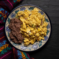 Scrambled eggs with green sauce and refried beans on dark background. Mexican food