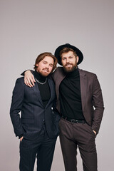 two guys in evening dress suits and hat posing smiling at camera, bearded caucasian men hugging, isolated in studio, portrait