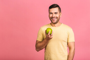 Diet concept. Cheerful beautiful young man eating apple, isolated over pink background.