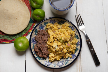 Scrambled eggs with green sauce and refried beans on white background. Mexican food