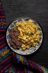 Scrambled eggs with green sauce and refried beans on dark background. Mexican food