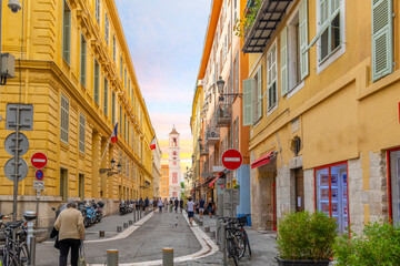 A one way street in the Old Town Vieux Nice section leading to the Rusca Palace Bell and Clock Tower as tourists enjoy the French Riviera.