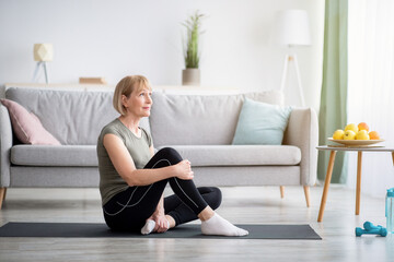 Attractive senior woman with slim body resting on yoga mat indoors, empty space