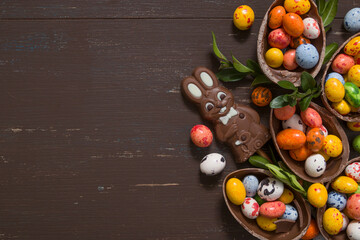 Easter hunt concept background with chocolate eggs and bunny on wooden table copy space. View from above