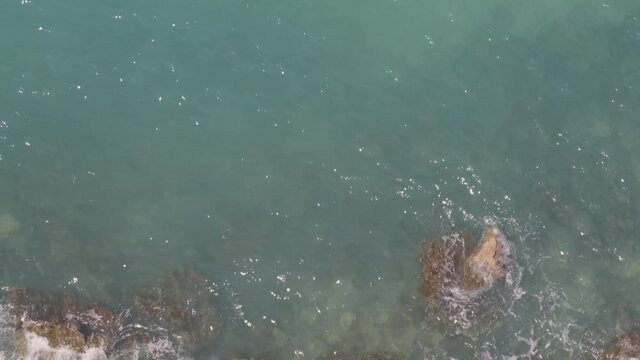 Top Down Aerial Pan from Waves Crashing on Rocks at Shore to Cliff in Greece