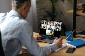 Online lesson. View over a man's shoulder at a laptop screen with different multiracial people and teacher gathered in an online lecture by video conference