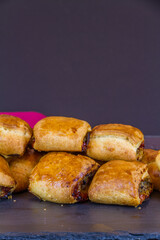 Home made sausage rolls on dark slate mat red napkin, portrait, copyspace, macro.