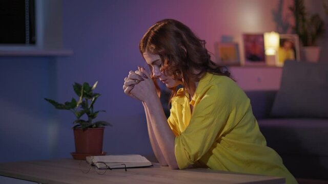 feeling hopeful, believing woman with hope and love prays with folded hands on her knees to God in room at night before bedtime