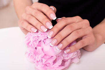 Beautiful female hands with bridal french manicure nails, pink and white gel polish, holding peonies flowers
