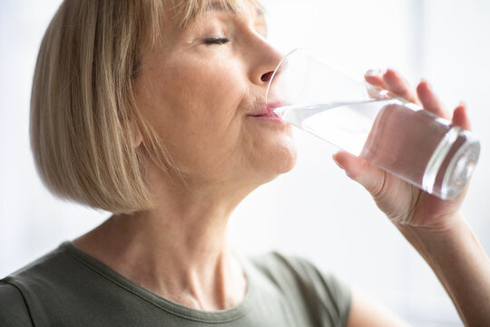 Portrait of sporty mature woman drinking water during her workout indoors. Healthy lifestyle concept