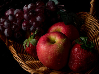 Fruit basket still life with fresh fruits in a wicker basket on black background with copy space