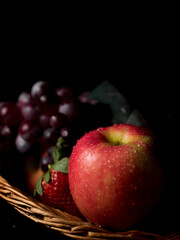 Fruit basket still life with fresh fruits in a wicker basket on black background with copy space