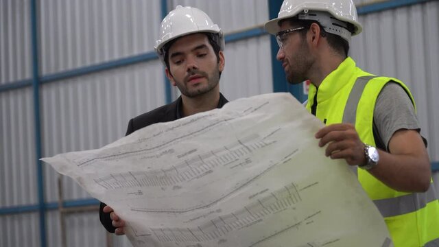 Executive business man or owner walking with foreman holding blueprint checking plans in construction site warehouse building indoors . worker drinking water. architect discussion with engineer
