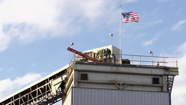 Slow Motion Wide shot of United States Flag Blowing in the Wind on top of Coal Stack at a Coal Mine in North America stock footage