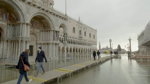 Tourists in face masks walking down temporary platform during flood in Venice