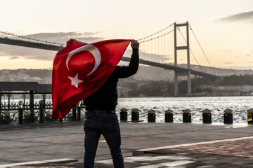 Man silhouette hold Turkish Flag in front of 15th July Martyrs Bridge (in Turkish 15 Temmuz Sehitler Koprusu ) or Bosphorus Bridge in Istanbul, Turkey. Patriotism concept.