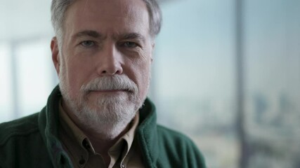 Portrait of an attractive senior adult male with a beard who smiles a little pleasant smile for the camera.