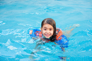 Kind mit Schwimmflügel und Schwimmweste im Schwimmbad