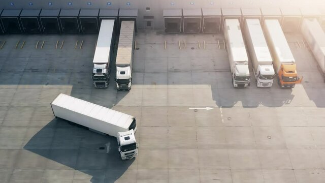 Semi truck with cargo trailer maneuvers along a parking lot of a warehouse in a logistics park. A lot of semi-trailers trucks stands at warehouses ramps for load and unload goods. Aerial view
