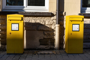 Zwei gelbe Briefkästen zwischen Sonne und Schatten stehen dicht vor einer Hausfassade. Ein Teil...