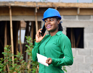 A Nigerian female construction and architectural engineer with blue safety helmet happily talking on phone 