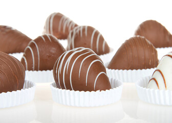Close up on giant strawberries dipped in white and milk chocolate, drizzled with contrasting white and milk chocolate. sitting in shallow white paper pastry dishes on reflective surface