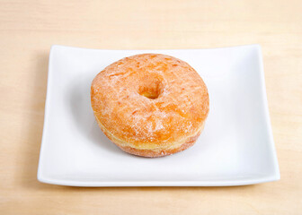 One round sugar coated donut on a rectangular porcelain plate on a light wood table.