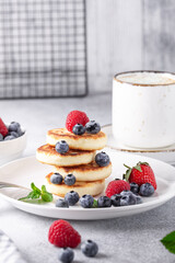 Stack of cheese pancakes with fresh berries, cup of coffee on the table. Tasty breakfast food. Vertical photo - Image