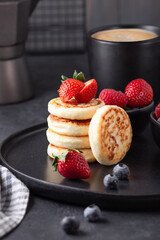 Close up of cheese pancakes with fresh berries on dark ceramic plate. Syrniki. Vertical photo - Image