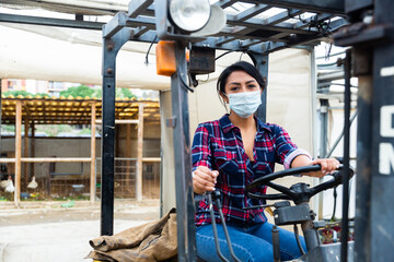 Fototapeta premium Latin american woman sits in a protective mask behind the wheel of a tractor autocar during a pandemic.