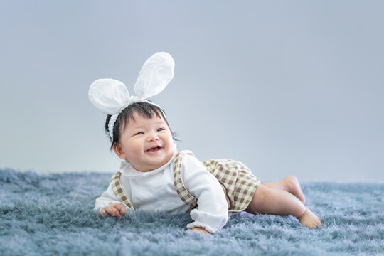 Baby in Easter bunny hairband. Asian happy baby crawling on carpet on gray background. Cute 6 months baby start crawling with copy space as Easter concept, baby or kid department in hospital