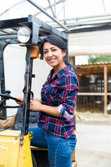 Fototapeta na wymiar Smiling hispanic woman working at the company gets behind the wheel of a forklift truck ...