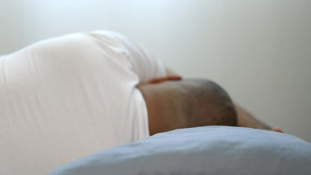 Asian bald man around the age of 30 in a white T-shirt can't sleep well. He has headaches, insomnia and nightmares.