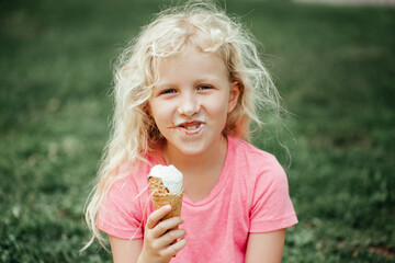 Cute funny adorable girl with dirty nose and milk moustaches eating licking ice cream from waffle cone. Child eating tasty sweet cold summer food outdoor. Summer frozen meal snack.