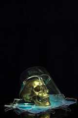 Golden skull with damage face protection on a small pile of disposable masks with a black background