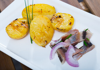 Fried potatoes with slices of mild-cured herring and onions served on plate at table