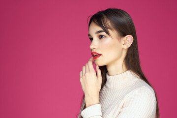 Brunette with long hair red lips cosmetics white sweater pink background cropped view