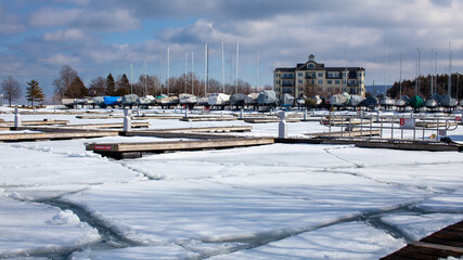 Sailboats line the perimeter of the Thornbury Yacht Club during the winter months when the harbor is frozen. The boats are winterized and covered up. The marina is frozen and the docks snowy.