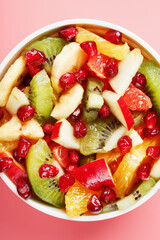 Fruit salad in a white cup on a pink background, free space for text.