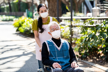 車椅子の高齢男性と介護福祉士の女性がマスクをして散歩している