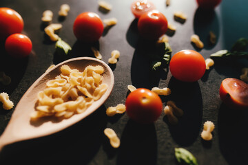 Cherry tomatoes, basil, butterfly vermicelli, wooden spoon, gray background